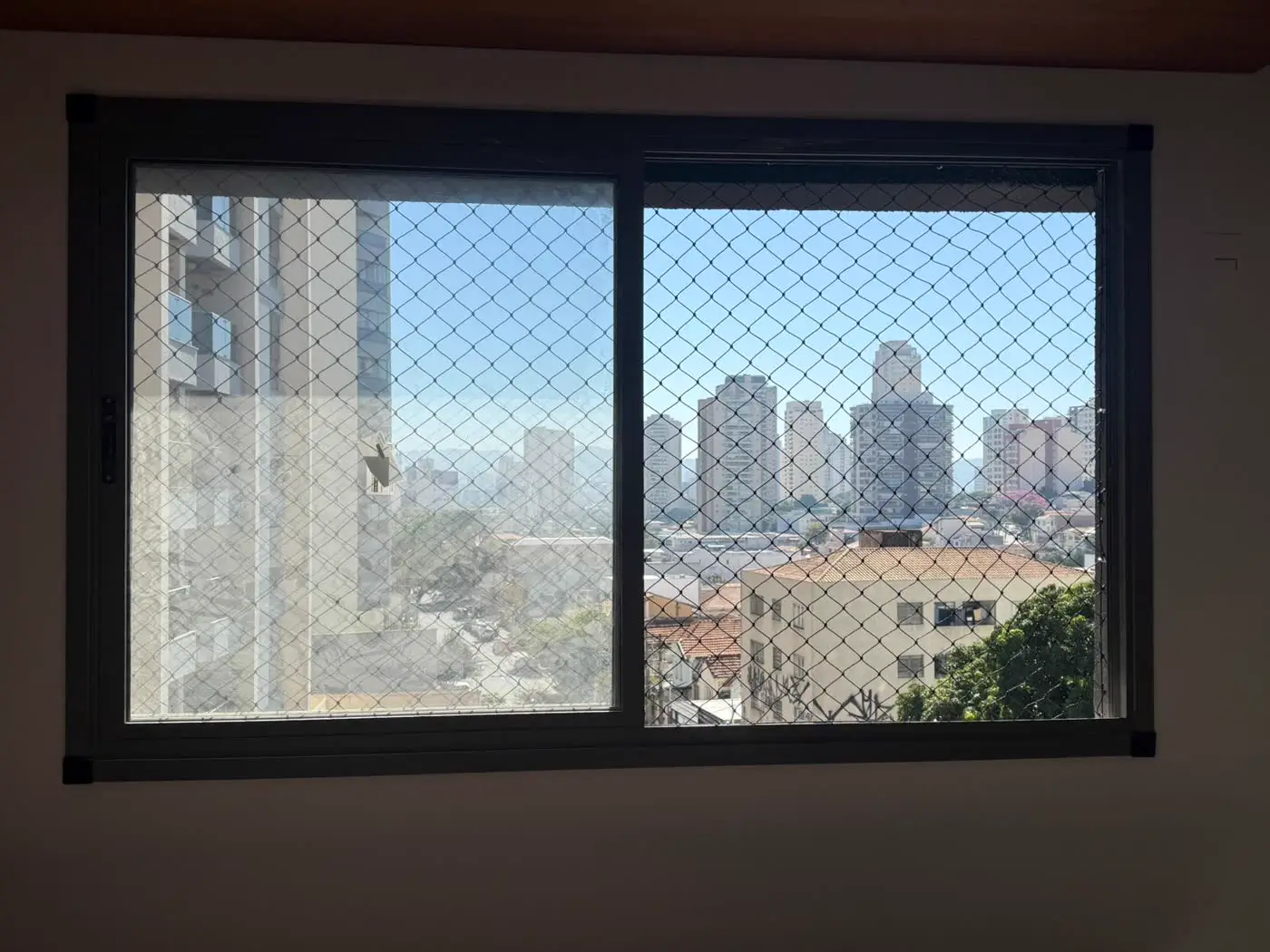 Janela panorâmica de apartamento com rede de proteção e vista da cidade