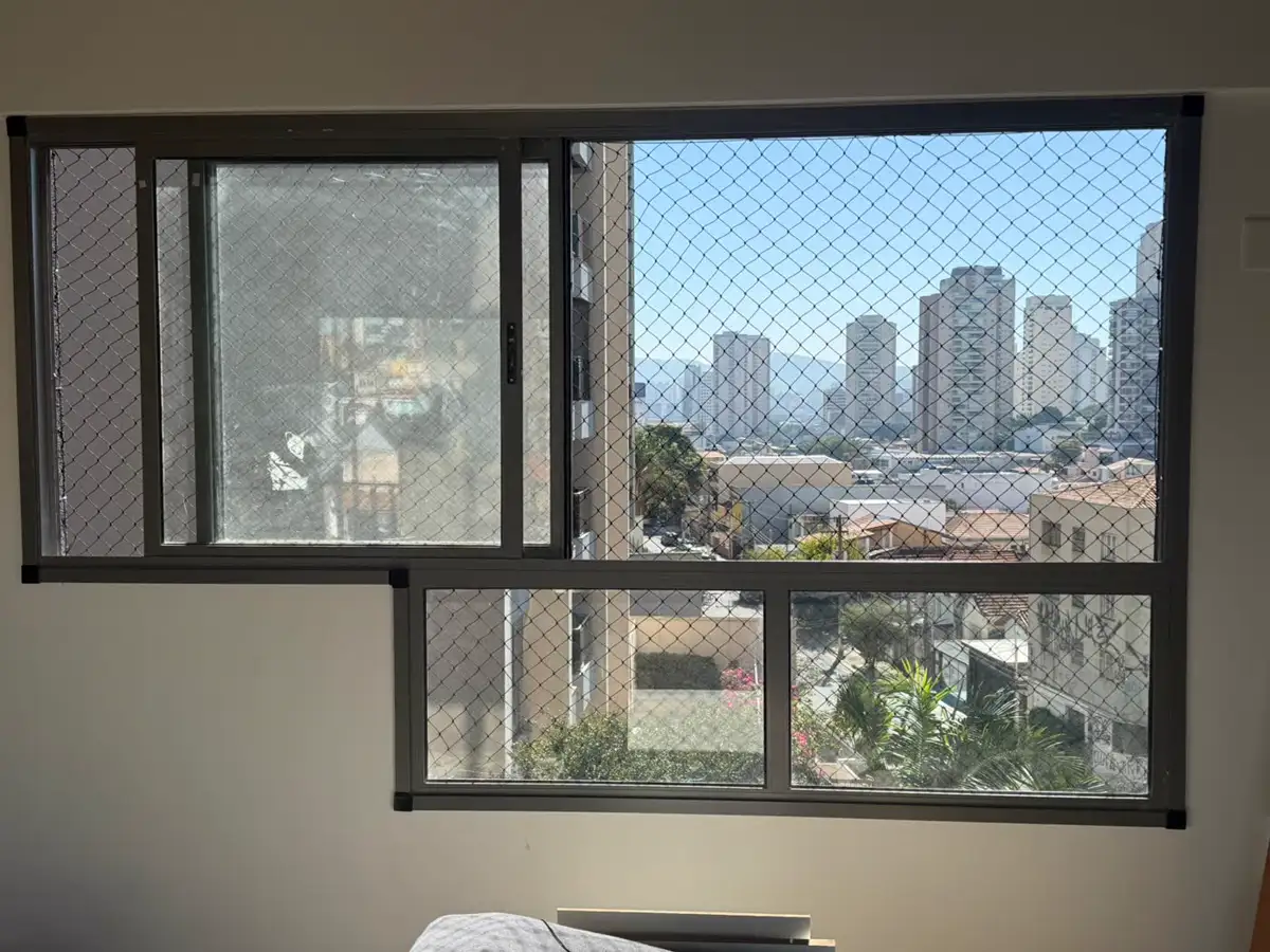 Janela ampla de quarto com rede de proteção fixada na esquadria